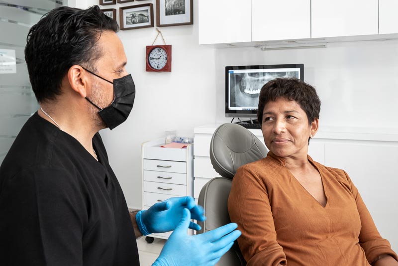 Dr. Omar, dentist in Cancun at SOTA Dental, speaks with a middle-aged female patient. He is wearing a make and she is listening intently.